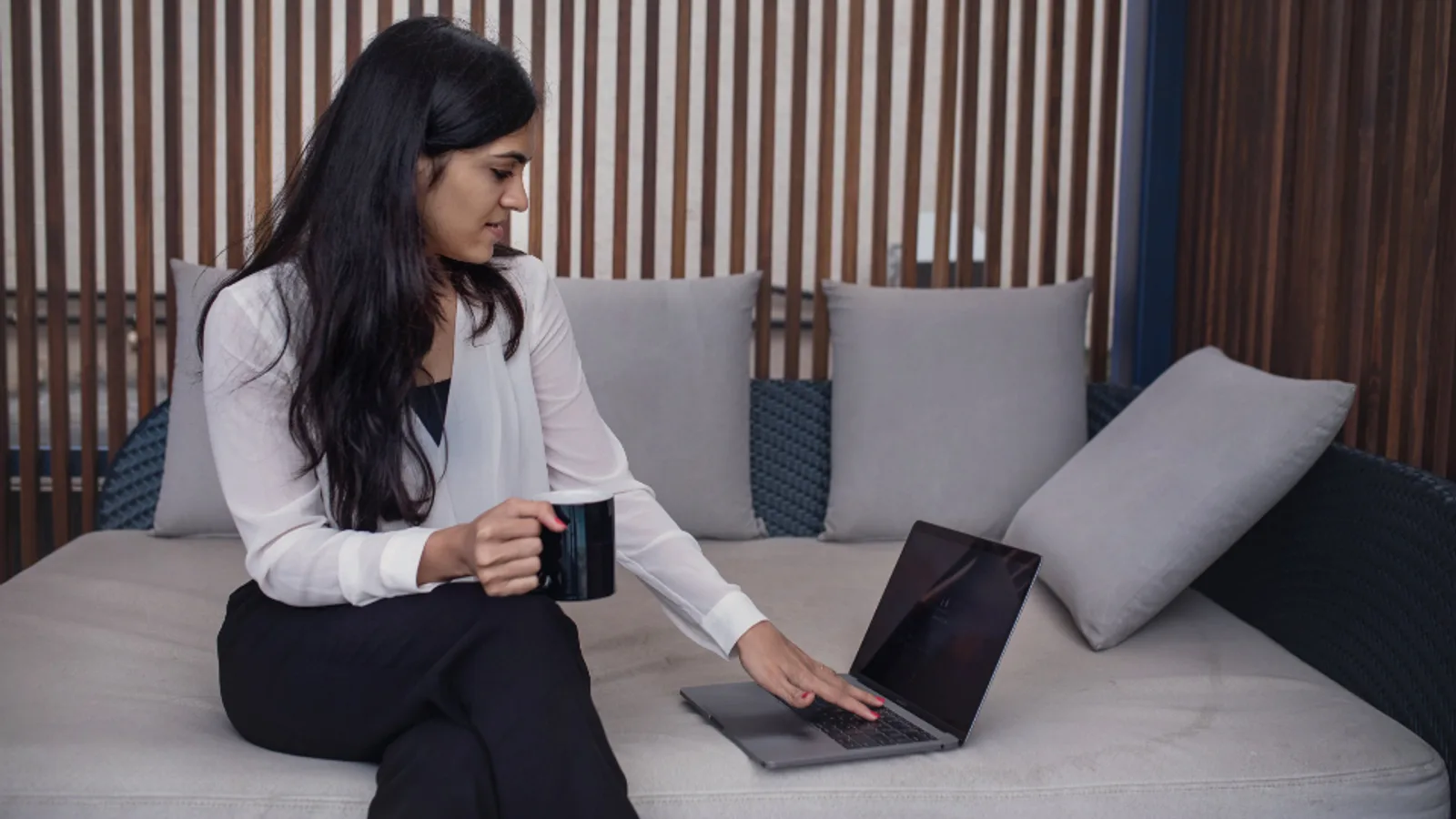 A woman working on a laptop from a sofa.