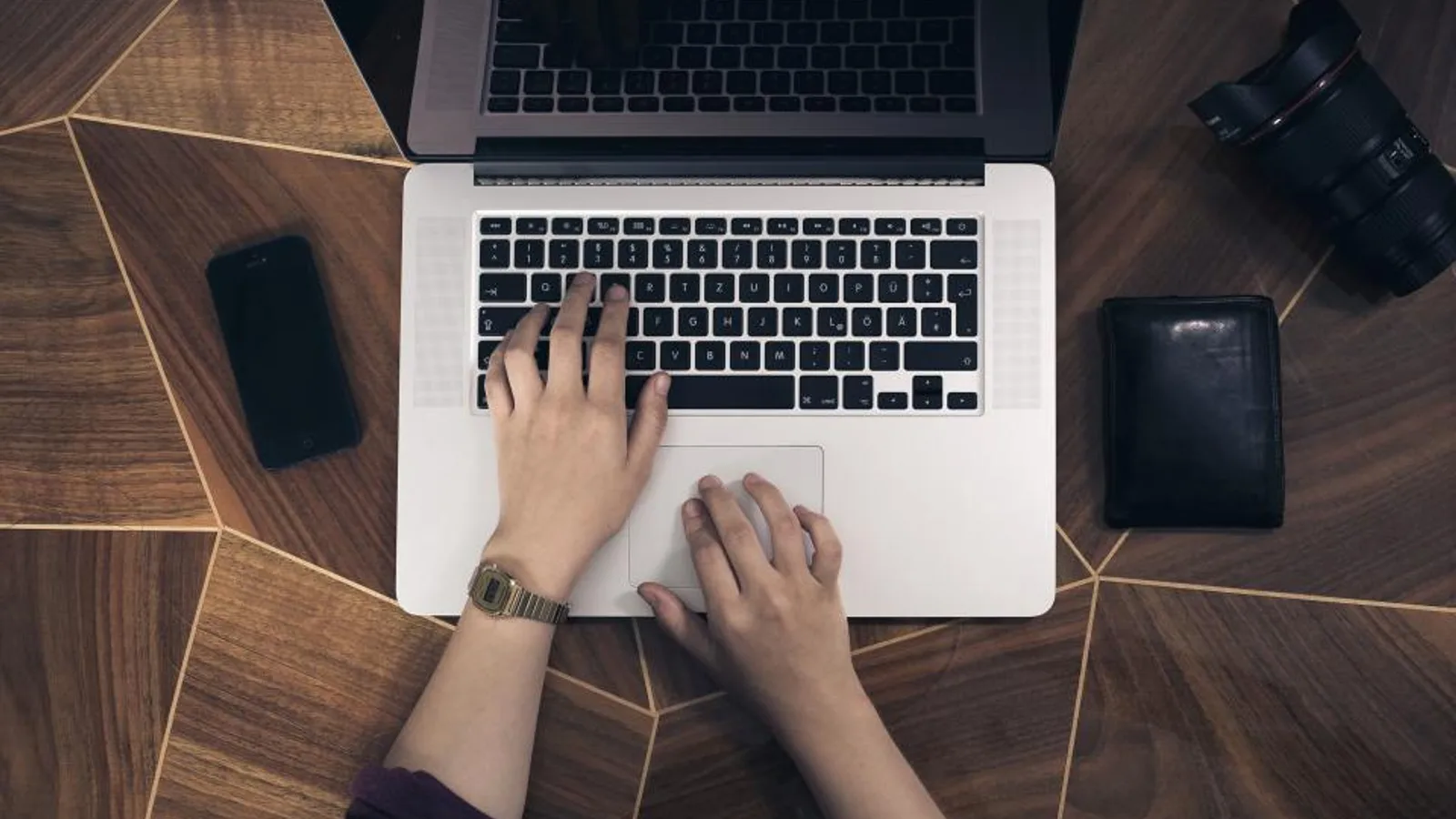 Overhead view of hands typing on a laptop beside a phone.