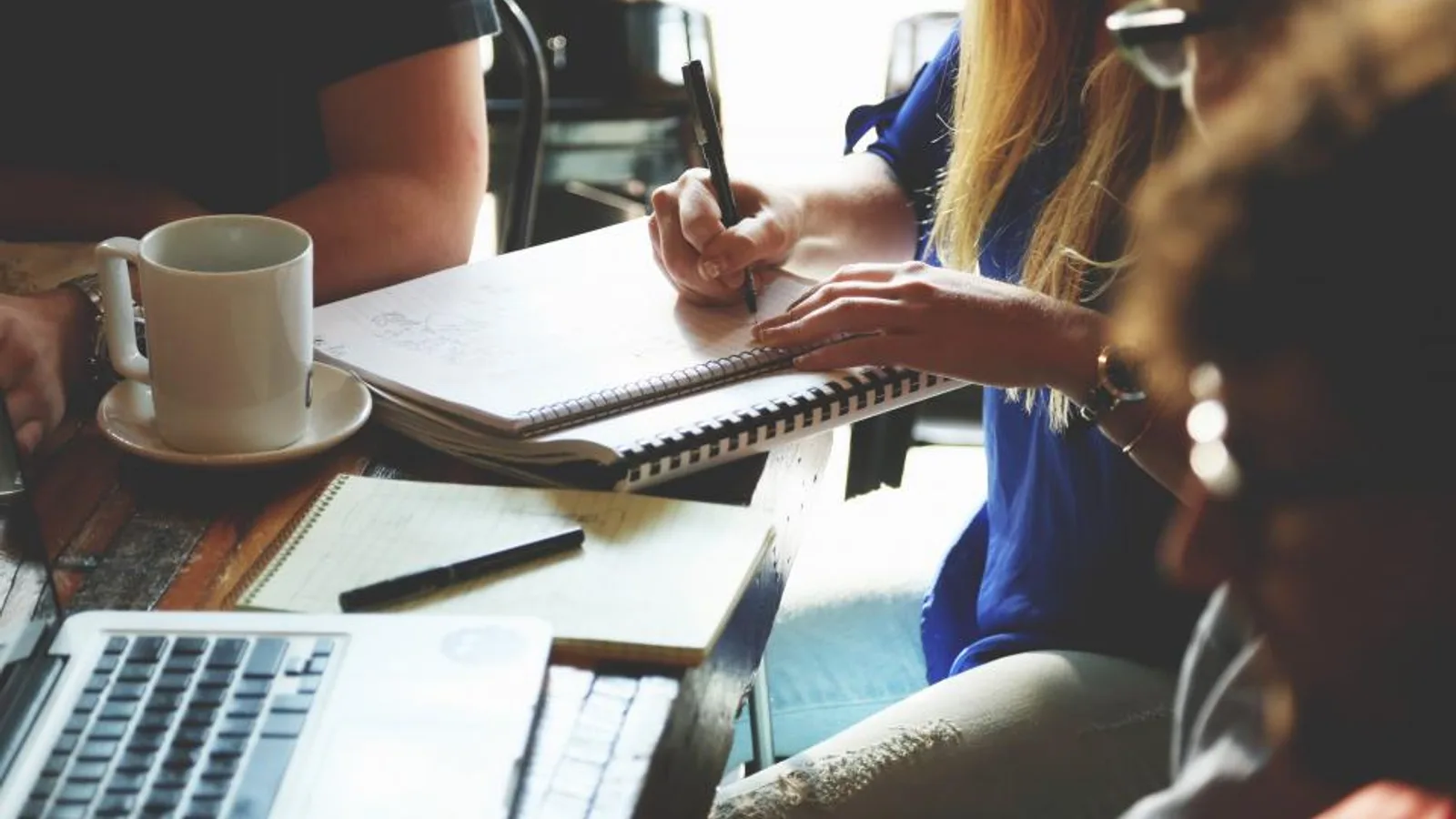 A team meeting around a table with notebooks and coffee.