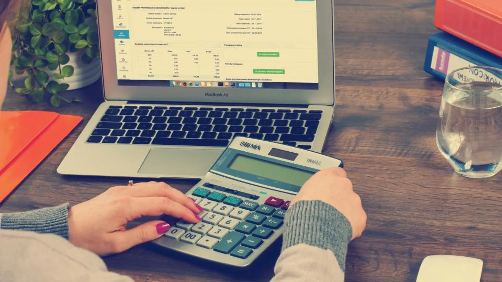 Hands using a calculator beside a laptop and financial paperwork.